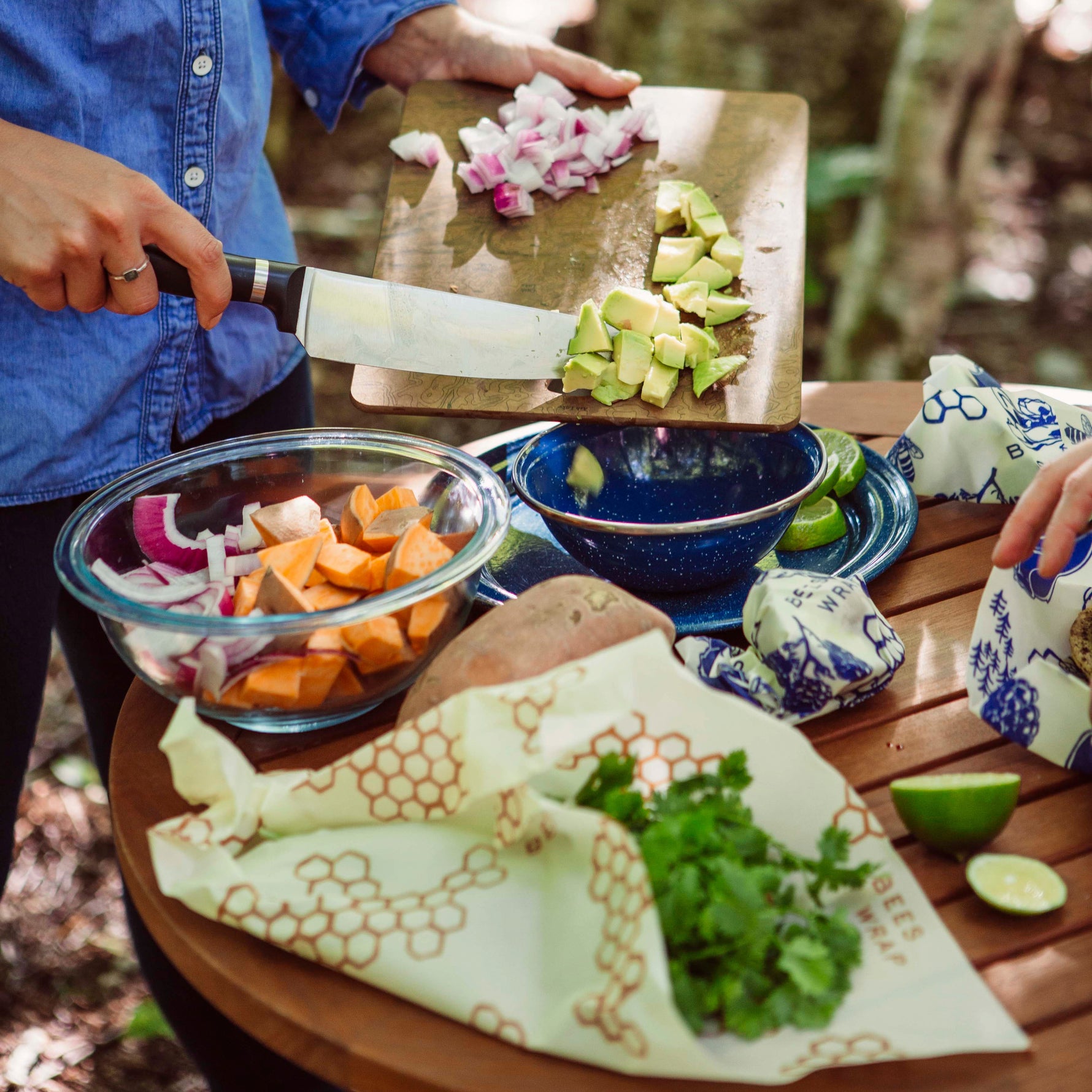 Person preparing food outdoors with a wooden table and natural background with vegetables wrapped in Honeycomb and Bees and Bears Bee's Wrap