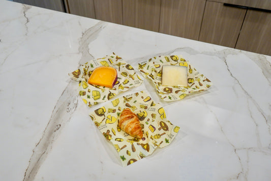 Bees Wrap Wheels n Wedges 3 pack in medium on a countertop with cheese and a croissant